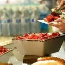 Two bowls of sliced strawberries and a plate of strawberries being held by someone