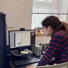 Woman leaning over a computer monitor that showed a pressed, dried plant