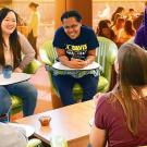 A diverse group of young people sitting together, laughing and engaging in conversation in a casual setting.. UC Davis Department of Plant Sciences
